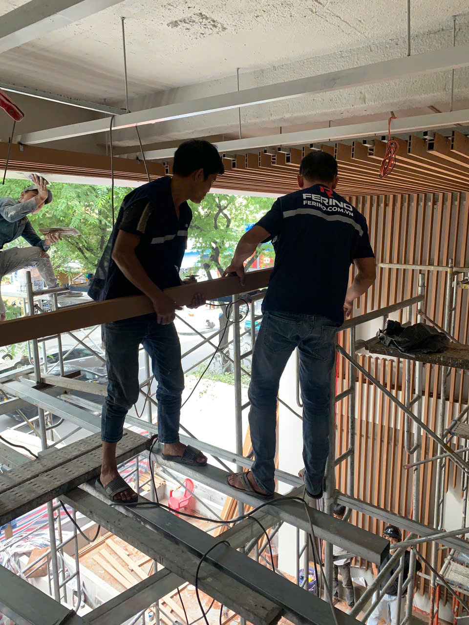 Đội thi công lắp thanh lam màu gỗ trên mặt tiền