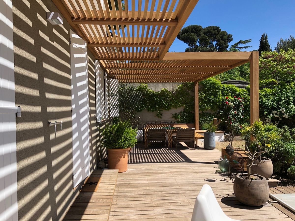Mái pergola lam gỗ tạo bóng đổ trên tường và sàn sân vườn